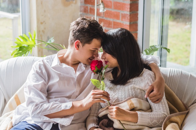 couple-embracing-on-a-couch-with-a-rose-in-their-hand_23-2147596352